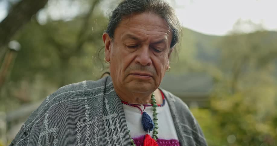 A man wearing native jewelry stands outside his home