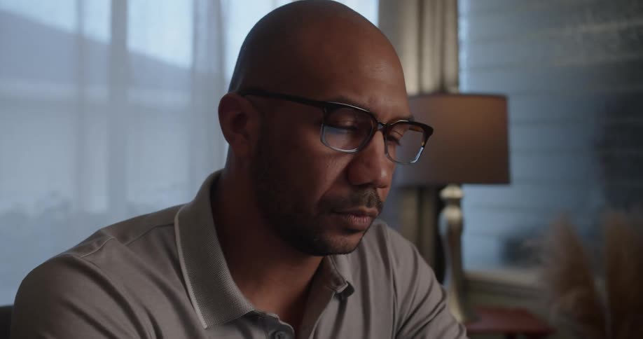 A man sitting indoors puts on his glasses before he begins to work