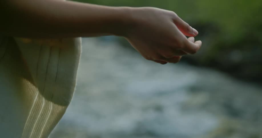 A close up of a womans hand with a flowing stream in the background as she brings her hands together in front of her face
