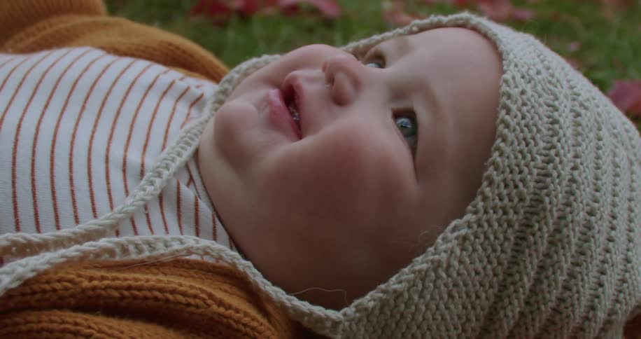 A close up of a babies face smiling as it lay on the grass