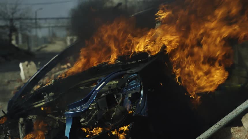 A close up of a burning vehicle in the streets of a run down city