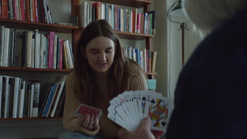 Younger and older women sit on floor near bookshelves playing cards