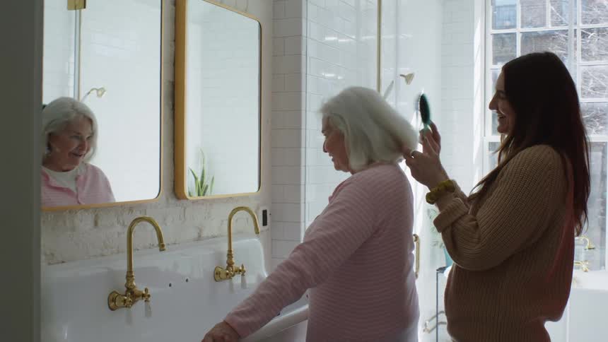 Young woman combs elderly womans hair in the bathroom