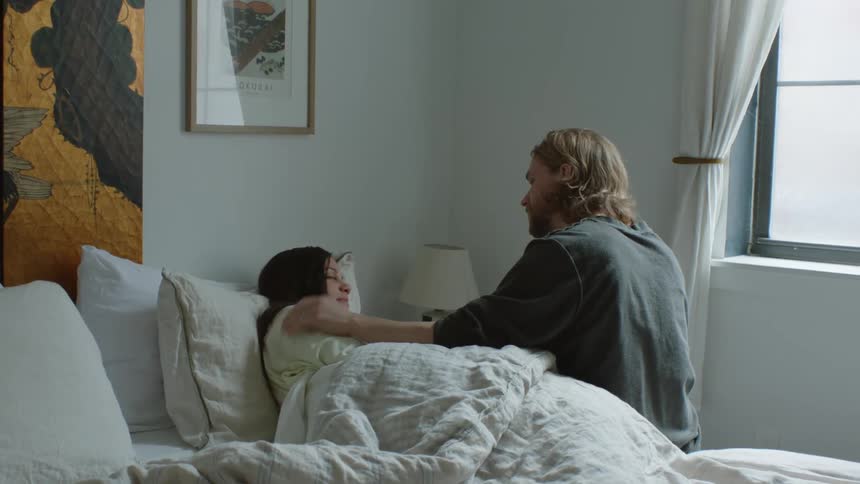 A husband strokes his wifes face while she lies sick in bed