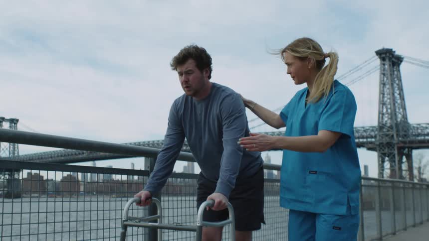A nurse helps a patient using a walker walk along a boardwalk