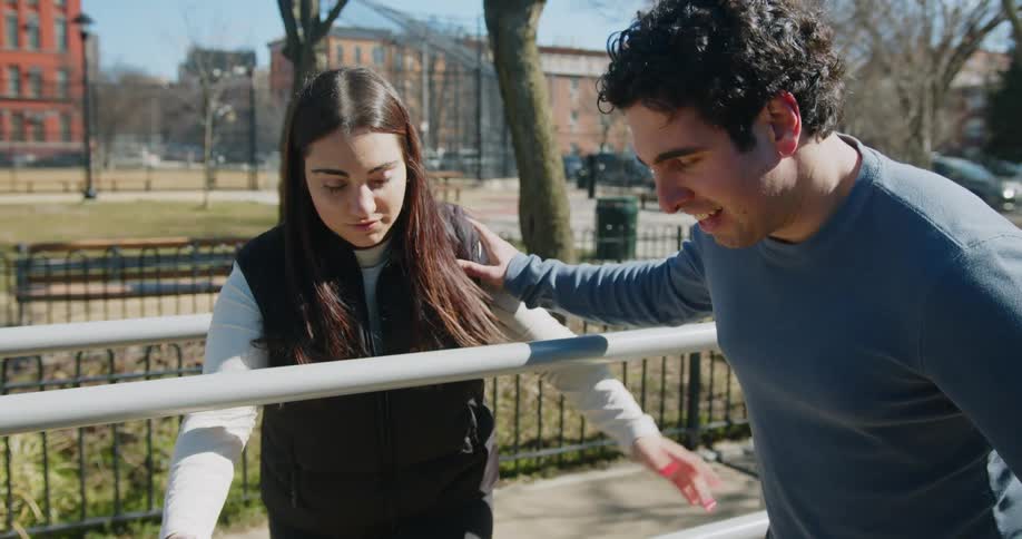 A woman walking next to a man who is walking between rails outside