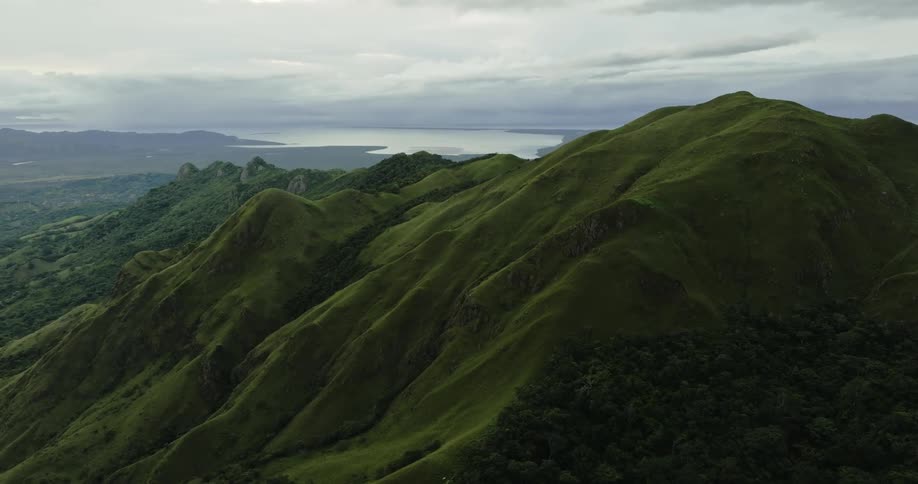 Aerial view of green mountain range with coastal area in the background