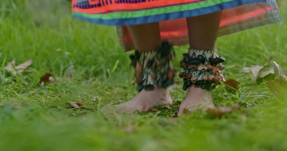 Close up of the feet of a woman wearing traditional native american clothes dancing in the grass