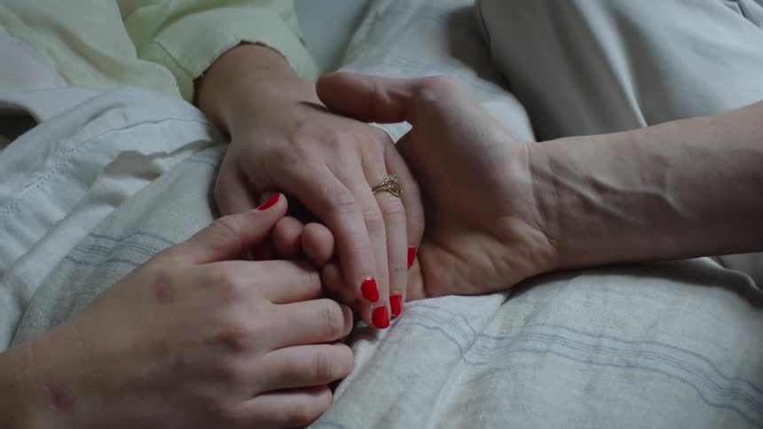 Close up of the hands of a couple gently holding each other in bed