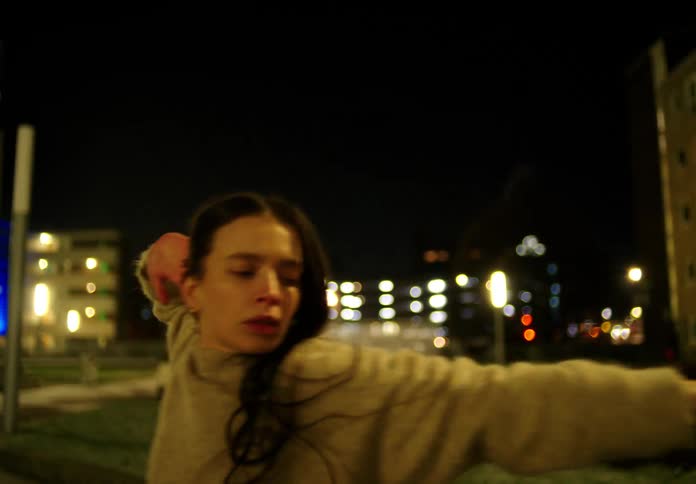 A woman moves her arms in the air as she dances on a street at night