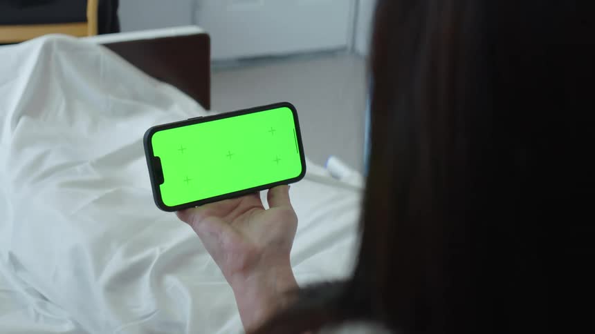 A person is holding their cell phone by the bed