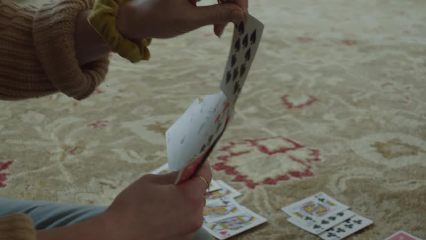 Close up of the hands of a woman playing cards over the rug in the living room