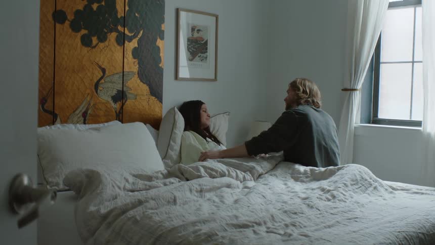 Husband kisses his sick wife in the forehead while she rests on bed