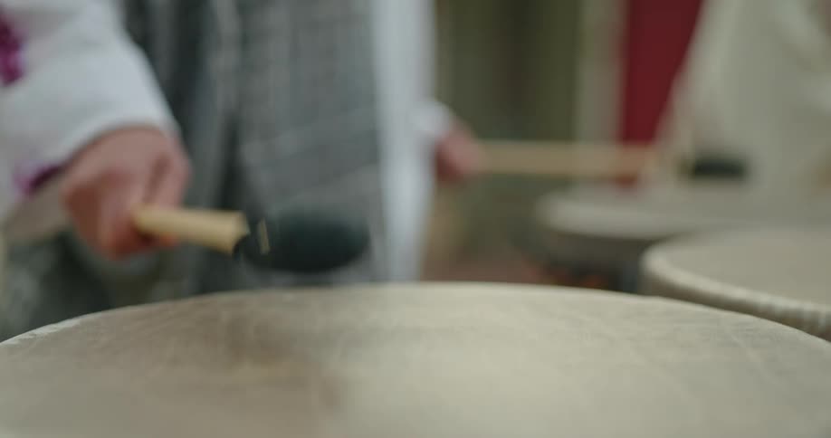 A person uses two long drumsticks to strike an array of large drums