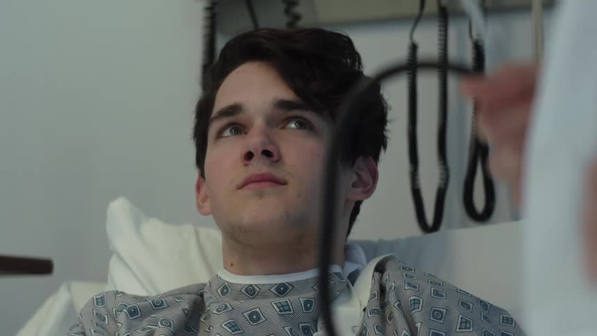 A teenage boy is lying in a hospital bed as he speaks to a doctor