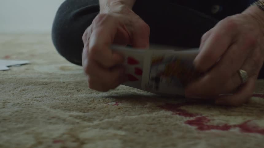 Close up of a person sitting over the rug in the living room shuffles cards
