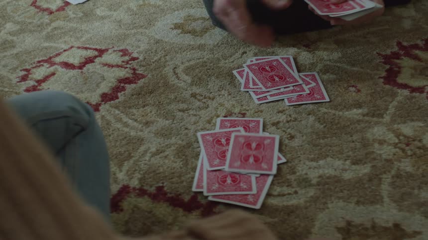 Two women are sitting on the floor playing cards on the carpet