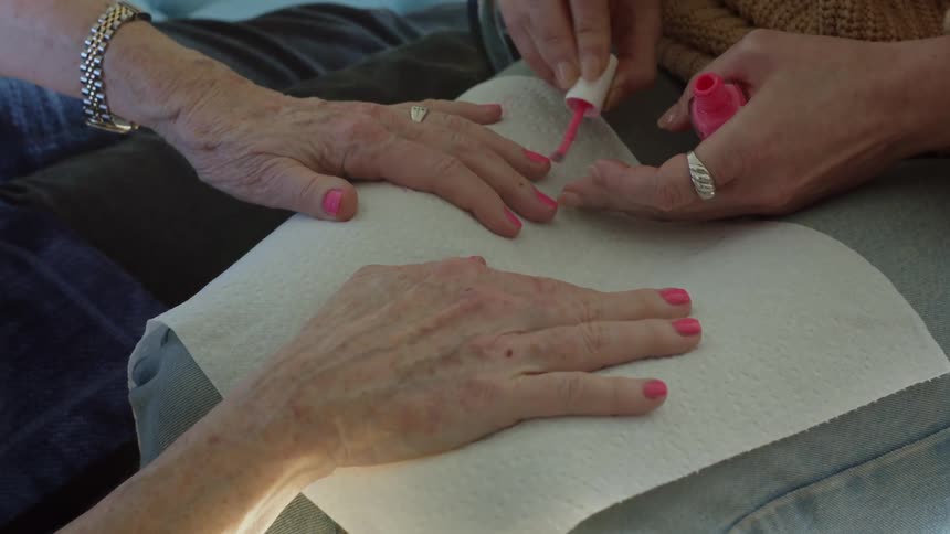 An up close of an elder womans hand whose nails are being painted pink