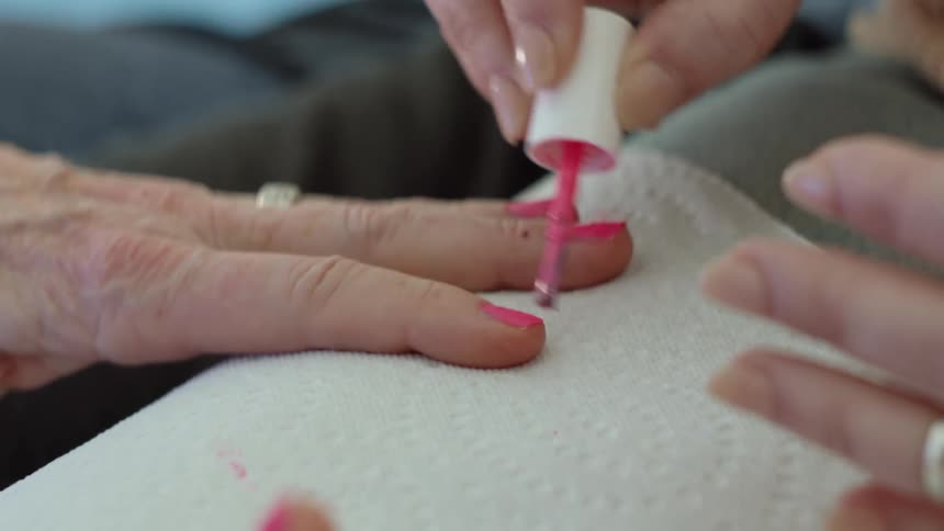 Close up of a woman applying nail polish on the fingertips of an elderly woman