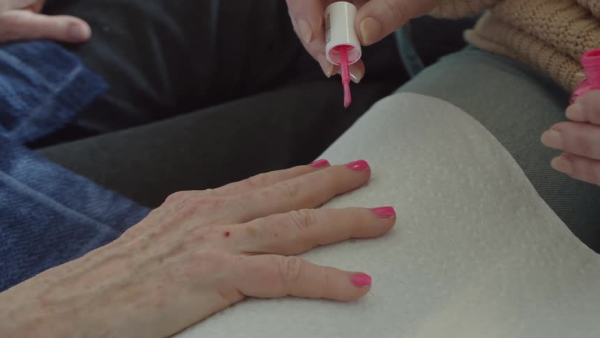 A woman paints an older womans nails with pink polish