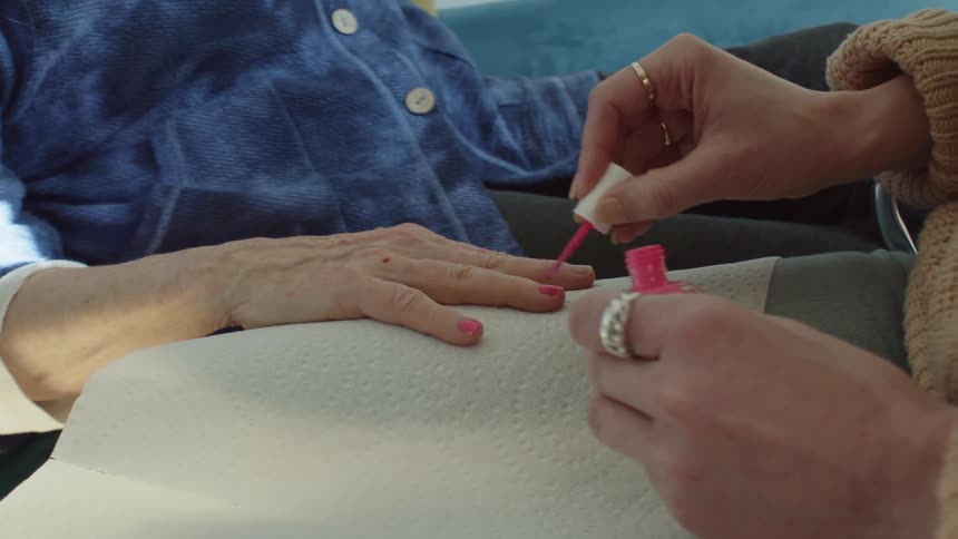 A woman paints another adults fingernails with bright pink nail polish