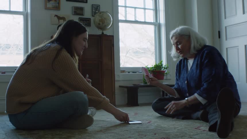 Two women are sitting on the floor playing a game of cards on the carpet