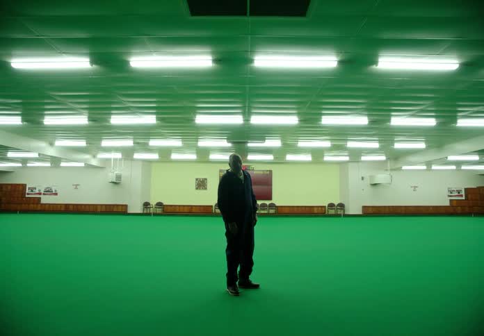 Man stands in the middle of a large room with bright green rug while the lights turn off