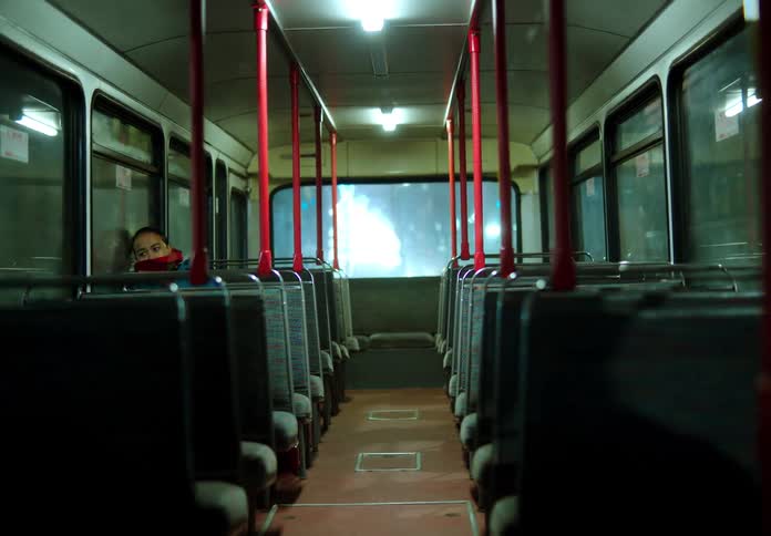 Woman with coat and red scarf travels on empty bus at night in the city