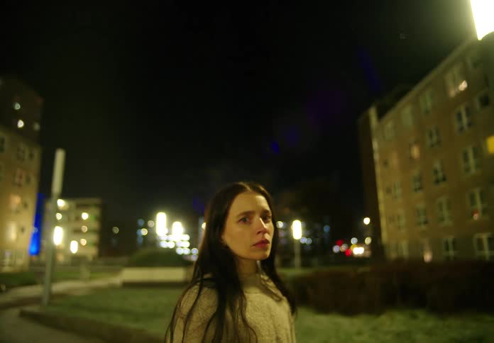 Young woman standing on walkway outside at nighttime looking fearful and backing away