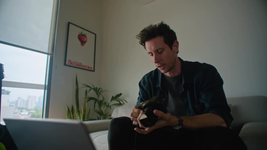 Young photographer inspects a camera while talking on a video call through a laptop