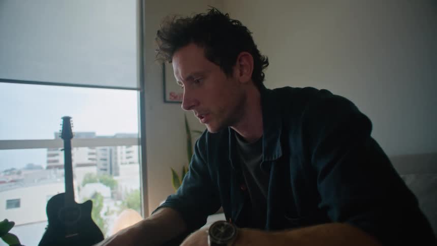 A man is sitting in his living room having a conversation with another man on his laptop computer