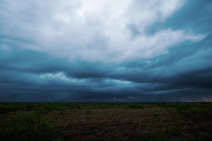 Bright blue and orange clouds moving over a large empty grassy area