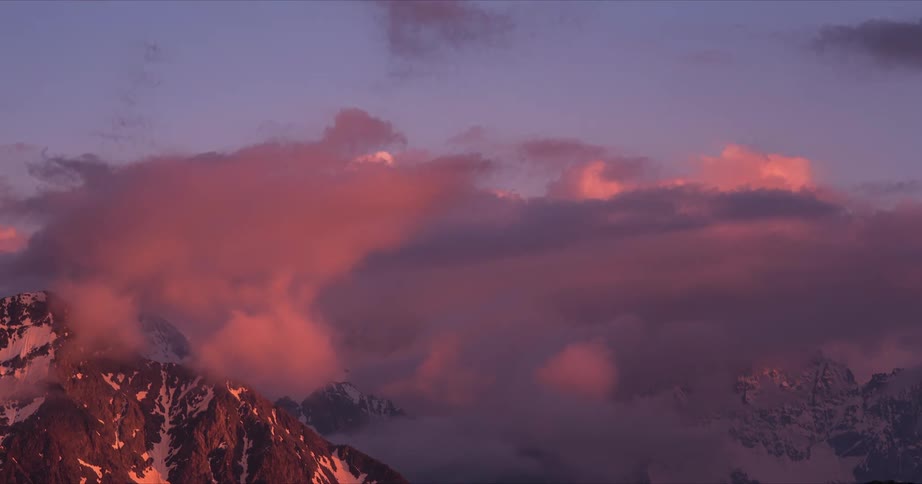 Time lapse of clouds shifting colors while rolling over the mountains at sunset
