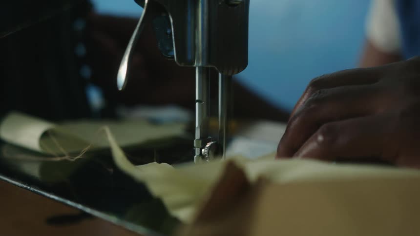A person feeding fabric through a sewing machine as it threads the fabric