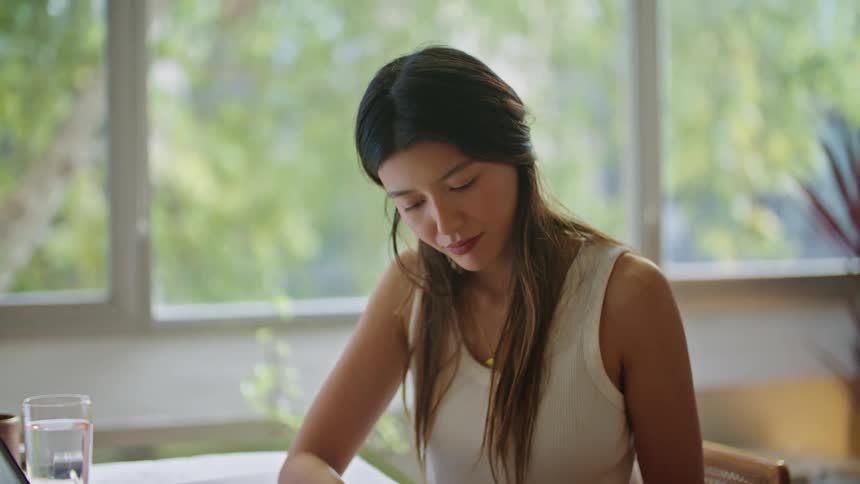 Woman with brown hair white shirt and jeans sits at desk works on plans and laptop at the office