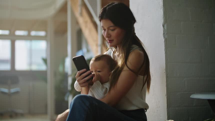 Woman uses smartphone while holding baby near staircase
