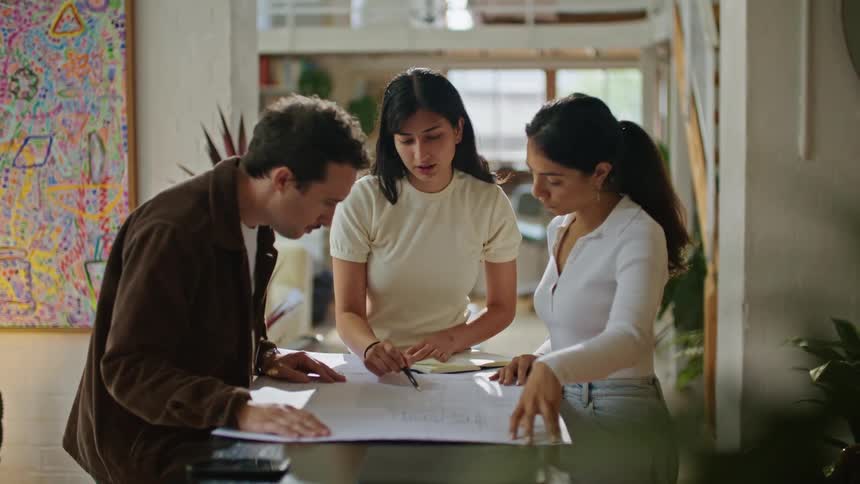 Man with mustache and brown jacket talks with women standing at table