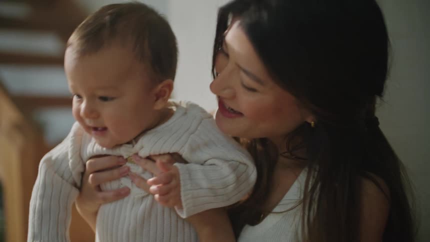 A woman bounces her baby while sitting at home