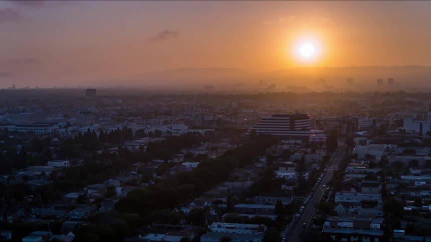 An aerial of a city with the sun rising over the horizon and fog settling over the distance