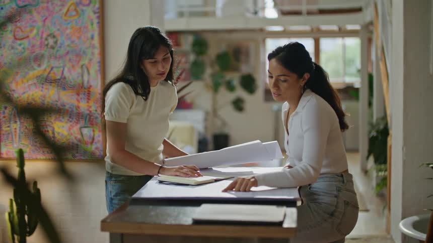 Two women discuss blueprints while standing at a table
