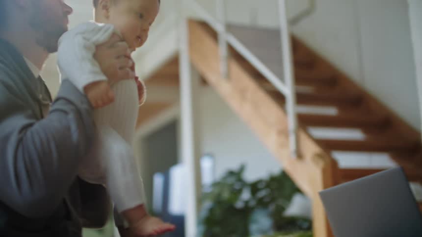 Mother is on laptop and dad is holding the baby inside