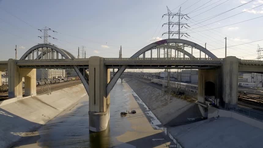 A panoramic view of a ditch under a bridge while a train rolls past