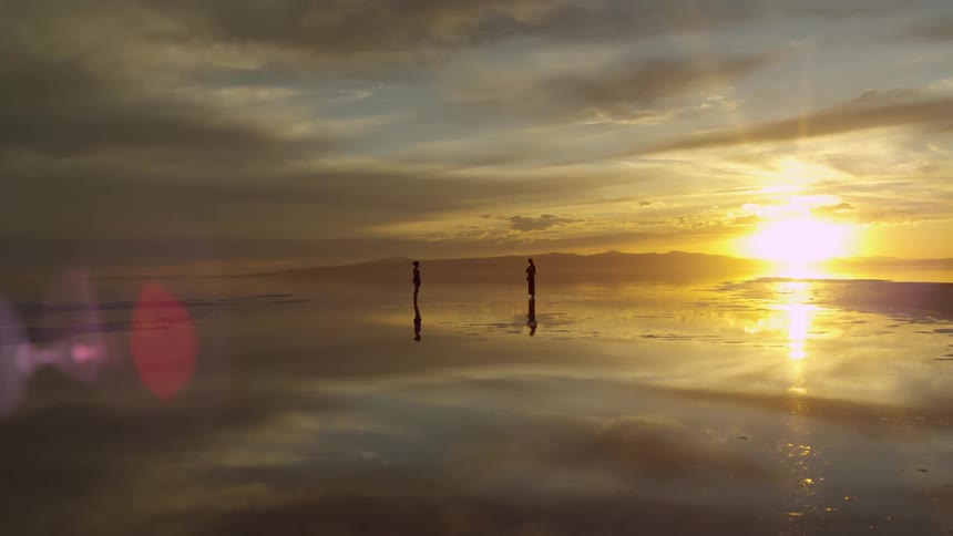 Two people stand on a beach at sunset