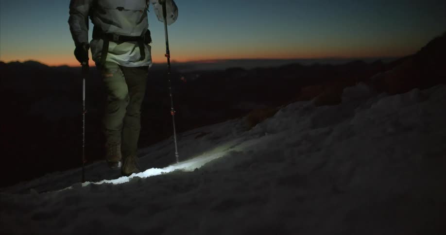 A man using walking poles makes his way across icy mountains at dusk