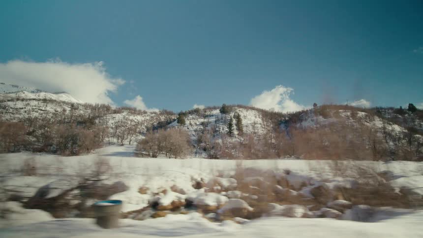 A fast moving image of a snow covered land with a stream near the snow bank and mountains in the distance