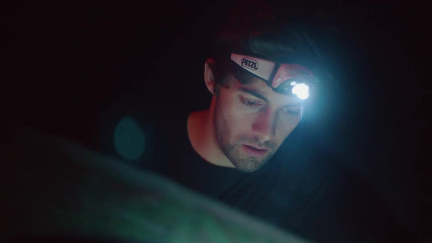 Man at nighttime wearing headlamp strapped to his head and looking at something in the dark