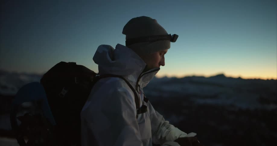 Man wearing backpack looks over mountainous terrain under a red horizon