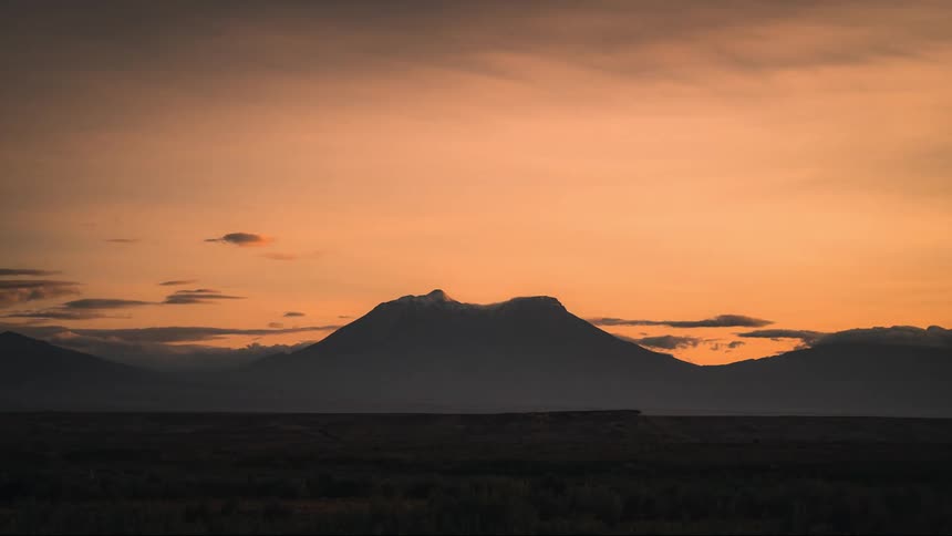 The sun rises over a mountain and flat field