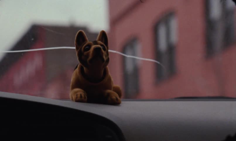 A bobblehead dog trinket sits on the dashboard of an automobile and shakes its head