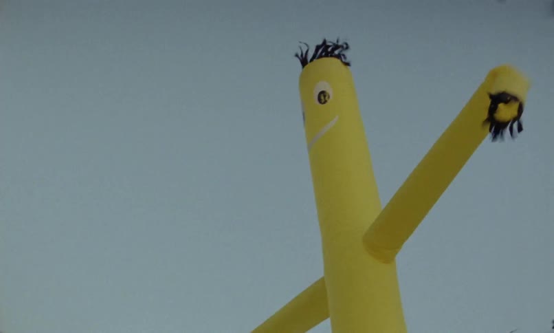 An inflatable balloon man waves in the wind under the open daytime sky